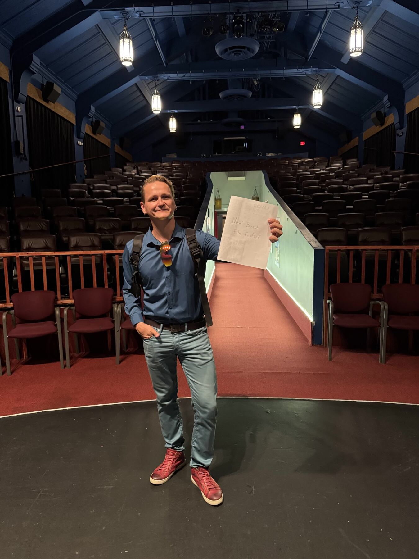 Festival visit on the stage of Savor Cinema, holding a sheet that reads Miami Beach Film Festival, auditorium behind